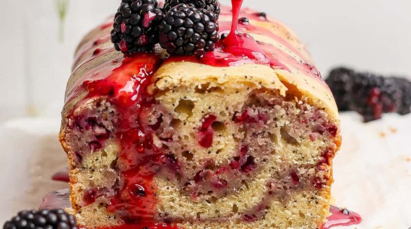 A loaf of blackberry bread topped with blackberries and a drizzle of blackberry sauce.