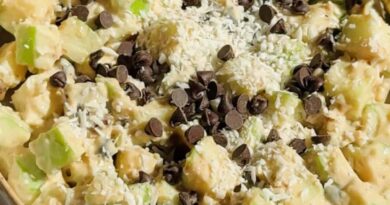 A bowl of chopped apples mixed with creamy sauce, topped with shredded coconut and chocolate chips, with a spoon on the side.