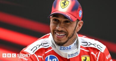 A smiling Lewis Hamilton wearing a Ferrari cap and race overall after he finished third in the Chinese Grand Prix