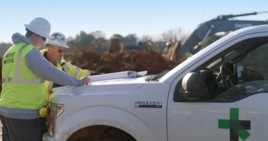 Two workmen look at plans on the hood of a Ford F150