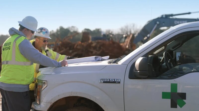 Two workmen look at plans on the hood of a Ford F150