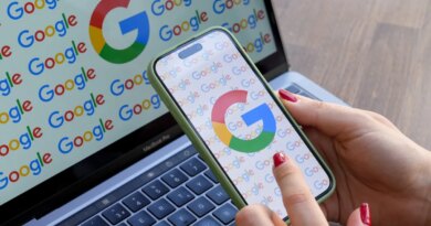 A woman looks at a mobile phone displaying the logo of Google in front of a laptop screen displaying the logo of Google.
