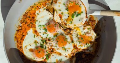 Fried eggs cooked in a skillet with tomato sauce and herbs, with a spatula lifting one egg.