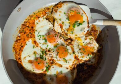 Fried eggs cooked in a skillet with tomato sauce and herbs, with a spatula lifting one egg.