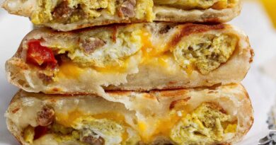 Three breakfast stuffed flatbreads stacked, filled with scrambled eggs, sausage, melted cheese, and some visible tomato pieces.