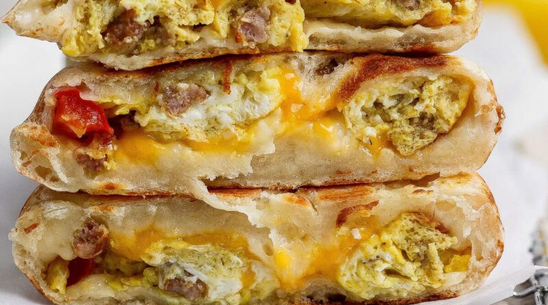 Three breakfast stuffed flatbreads stacked, filled with scrambled eggs, sausage, melted cheese, and some visible tomato pieces.
