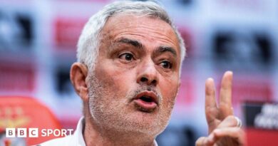 Close-up of Jose Mourinho speaking at a press conference. He has short grey hair, brushed to his right, and stubble. He is gesturing with his left hand.