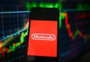 Nintendo logo is seen displayed on a smartphone with stock market percentages on the background.