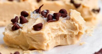 A creamy peanut butter fudge piece topped with chocolate chips and flaky salt, showing a bite taken out, resting on parchment paper.