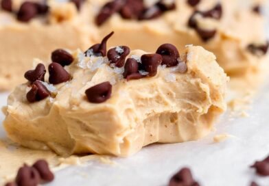 Peanut Butter Frozen Yogurt Bites A creamy peanut butter fudge piece topped with chocolate chips and flaky salt, showing a bite taken out, resting on parchment paper.