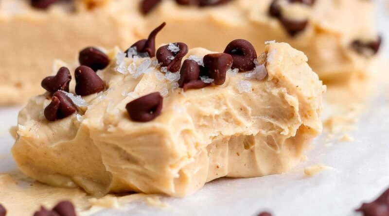 A creamy peanut butter fudge piece topped with chocolate chips and flaky salt, showing a bite taken out, resting on parchment paper.