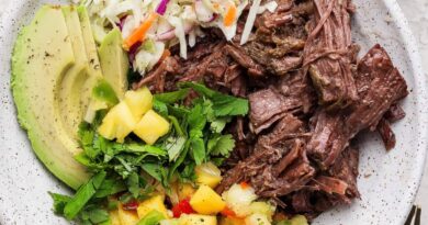 A bowl containing shredded beef, sliced avocado, coleslaw, chopped cilantro, and pineapple salsa.