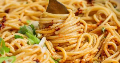 A fork twirls spaghetti coated in a creamy, orange-hued sauce with green onions sprinkled on top.
