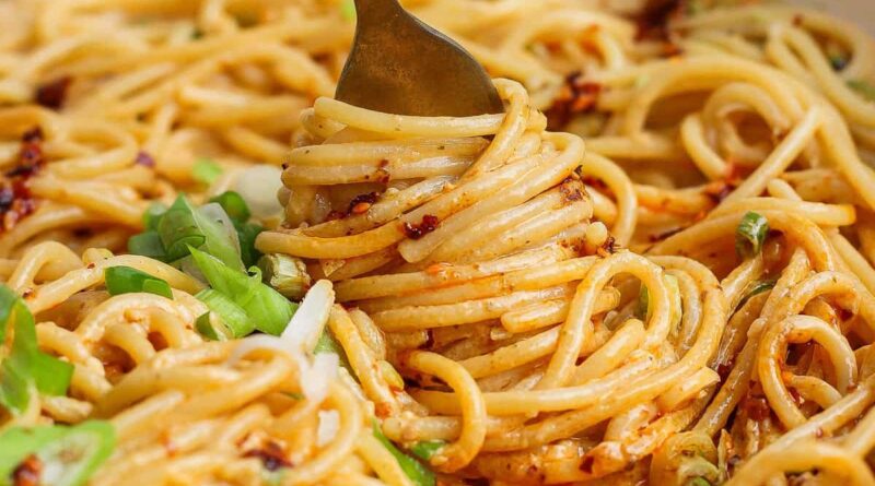 A fork twirls spaghetti coated in a creamy, orange-hued sauce with green onions sprinkled on top.