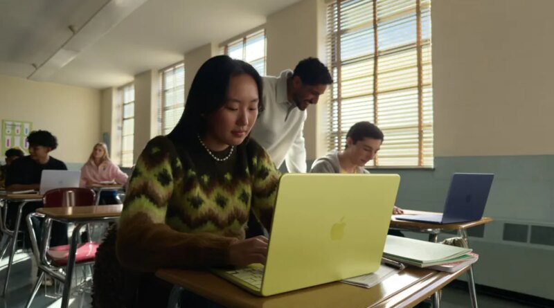 young woman seated at a classroom desk using a MacBook Neo