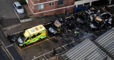 An aerial photograph showing three blackened and burned out ambulances and one badly damaged one, parked outside a building.
