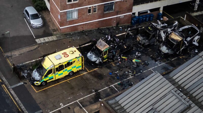 An aerial photograph showing three blackened and burned out ambulances and one badly damaged one, parked outside a building.