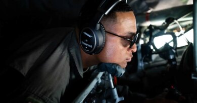 A man in uniform inside a plane, wearing sunglasses and headphones.