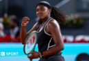 Hailey Baptiste, wearing a black vest and shorts, black headband and a ponytail, holds her green Wilson racket in her left hand and punches her right fist in celebration