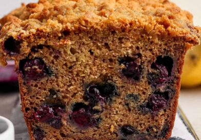 Close-up of a sliced loaf of blueberry banana bread with a crumbly topping, showing visible blueberries inside the moist bread.