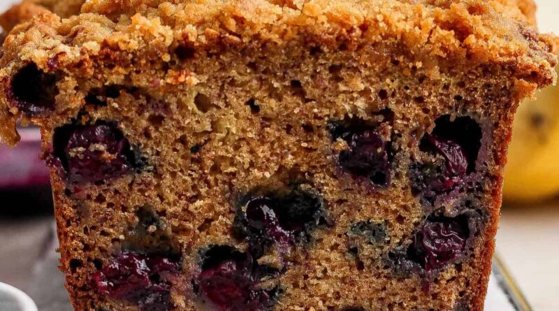 Close-up of a sliced loaf of blueberry banana bread with a crumbly topping, showing visible blueberries inside the moist bread.