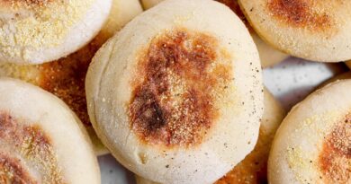A close-up photo of several golden-brown English muffins sprinkled with cornmeal.