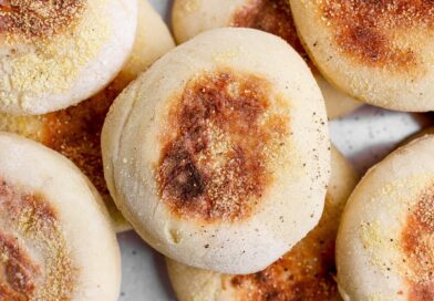 A close-up photo of several golden-brown English muffins sprinkled with cornmeal.