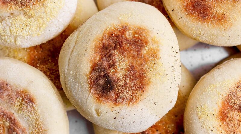 A close-up photo of several golden-brown English muffins sprinkled with cornmeal.