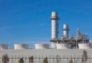 Smoke stacks from a natural gas power plant stand against a blue sky.