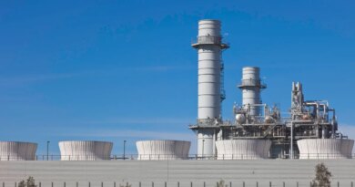 Smoke stacks from a natural gas power plant stand against a blue sky.