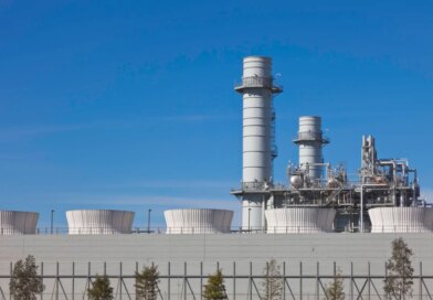 Smoke stacks from a natural gas power plant stand against a blue sky.