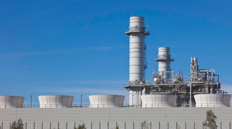 Smoke stacks from a natural gas power plant stand against a blue sky.