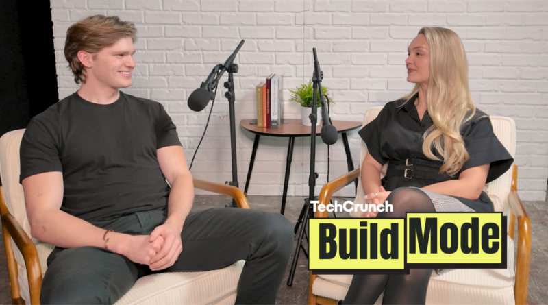 Artisan CEO, Jaspar Carmichael-Jack and Build Mode host Isabelle Johannessen sit facing each other in a podcast studio with microphones, mid-conversation, in front of a white brick wall; a small table with books and a plant sits between them, and a “TechCrunch Build Mode” logo overlay appears in the lower right corner.