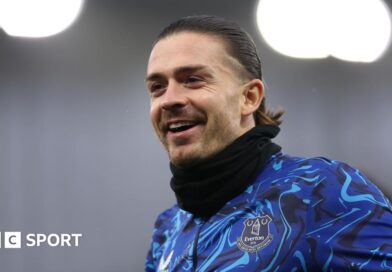 Jack Grealish poses for a photo with five athletes from Special Olympics Great Britain. They are all holding up Everton shirts with '26.2' on. 