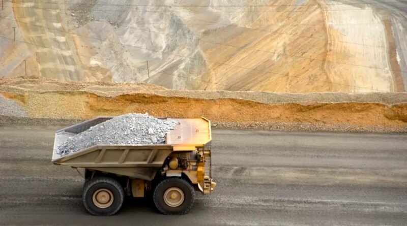 A large yellow dump truck carries ore out of a pit mine.