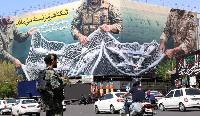 epa12870206 A member of the Iranian security forces watches over traffic passing a huge political billboard reading in Persian ’The Strait of Hormuz will remain closed', in Enghelb square in Tehran, Iran, 05 April 2026. Iran's Revolutionary Guards (IRGC) said a US aircraft that had been searching for the crew member of a missing US fighter jet had been destroyed, Iranian media reported on 05 April 2026. EPA/ABEDIN TAHERKENAREH