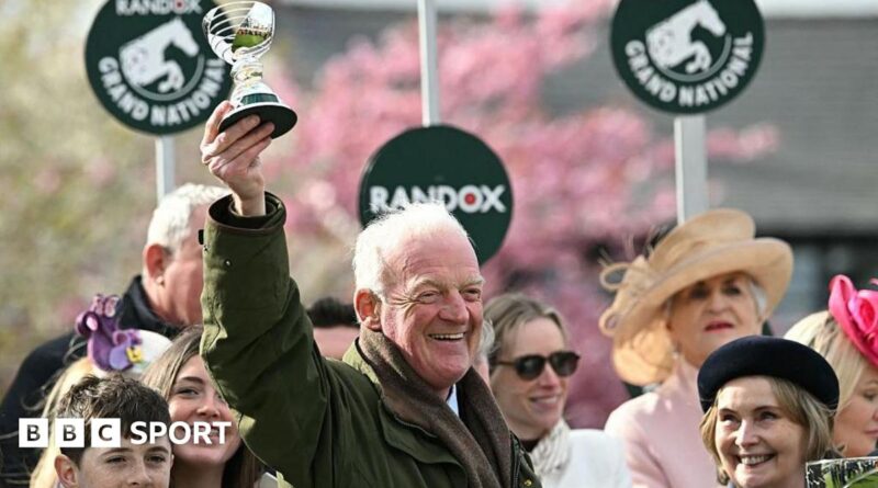 Willie Mullins smiling and holding a trophy in the air