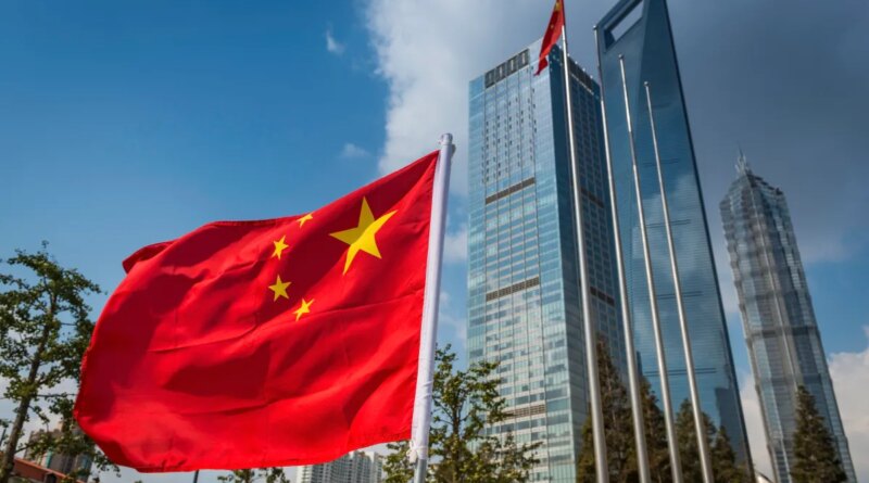 The vibrant red field and yellow stars of the Flag of the People's Republic of China flying in the breeze beside the futuristic glass and steel towers of Pudong's soaring skyscrapers, Shanghai, China.