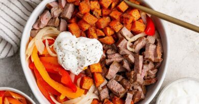 A bowl filled with diced steak, roasted sweet potatoes, saut&eacute;ed onions and bell peppers, topped with a dollop of sour cream and black pepper, with a fork resting inside.