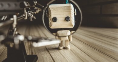 Wooden Robot Android Stands On A Table Under A Magnifying Glass. Metal Clamps With Magnifying Glass