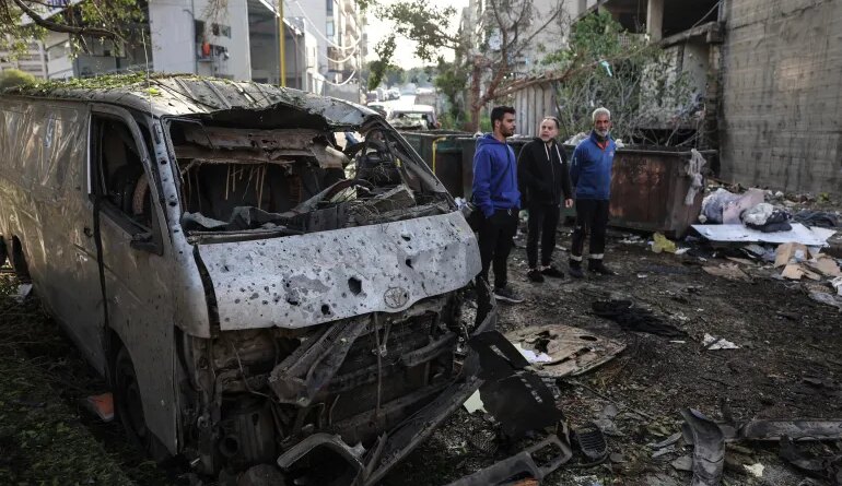 Men look at the damage next to the wreckage of a vehicle at the site of an Israeli strike in Beirut on April 1, 2026.
