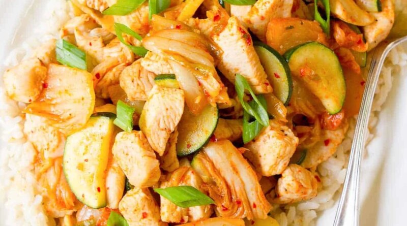 Kimchi chicken stir fry and rice on a white plate.