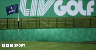 A flag on a golf course green in front of a sign that says 'LIV Golf'