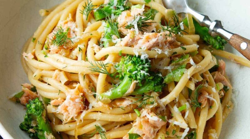 Bucatini noodles with salmon, broccoli and dill in a white bowl.