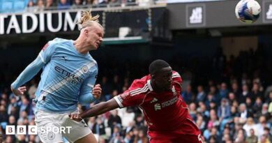 Erling Haaland, wearing Manchester City's light blue kit, celebrates his latest hat-trick by making a three-finger salute with his left hand