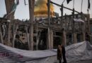 People look at a destroyed building within the Grand Hosseiniyeh, with the mosque visible in the background, after it was hit in airstrikes. 