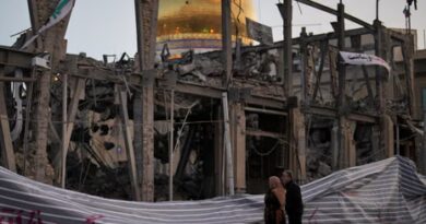 People look at a destroyed building within the Grand Hosseiniyeh, with the mosque visible in the background, after it was hit in airstrikes. 