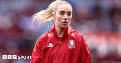 Missy Bo Kearns wearing a red jacket with an Aston Villa badge on the chest