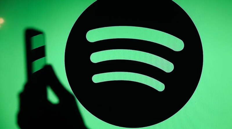 The Spotify logo displays on a screen with a person holding a phone.
