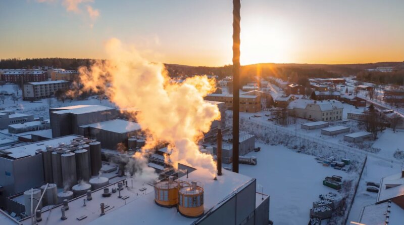 Aerial view of an industrial building in winter with sun lit smoke / steam rising up from the chimneys.